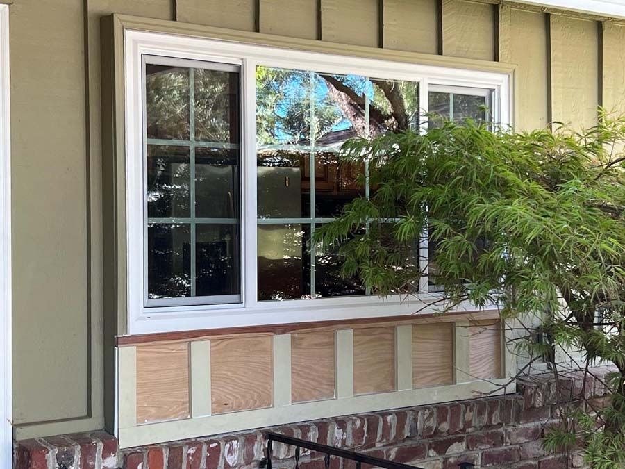 Close-up of a house window with vertical grid patterns, featuring energy-efficient, multi-pane glass that meets California Title 24 windows standards. The window has a light-colored frame and sits above a green-painted sill.